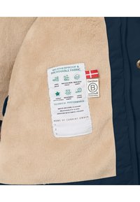 Beige Fleece-Futter mit einem marineblauen Außenmaterial. Das Etikett zeigt witterungsbeständige Eigenschaften, einschließlich Isolations- und Atmungsaktivitäts-Bewertungen.