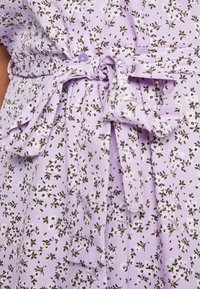 Vestido lilás com padrão floral, apresentando um cinto amarrado na cintura, botões redondos e um tecido leve e texturizado.