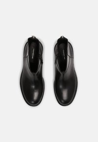 Černé kotníkové kožené boty s hladkou texturou, pružnými bočními panely a stříbrným zipem na zadní straně. Pevná gumová podrážka.