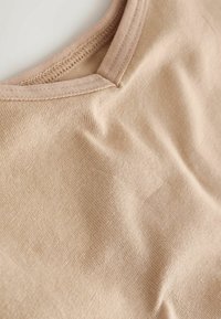 Gros plan sur un tissu beige présentant un col rond avec une double couture et une texture en maille fine et lisse.