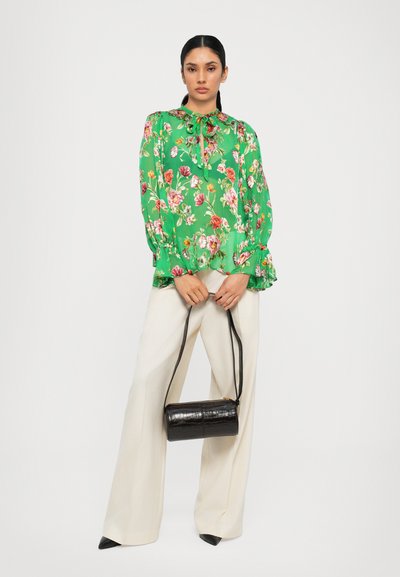Green floral blouse with long sleeves, gathered cuffs, and a neck tie. Paired with cream wide-leg pants and a small black textured handbag.