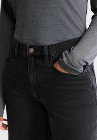 Černé džíny z denimu s vysokým pasem, pěti kapsami a měděnými knoflíky, doplněné šedým vrškem s dlouhým rukávem a žebrovým vzorem.