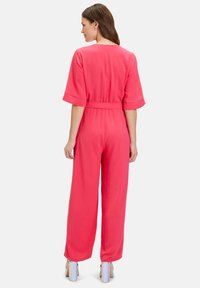 Bright pink, short-sleeve jumpsuit with a relaxed fit, cinched waist, and wide legs. Features smooth, textured fabric and flared sleeves.