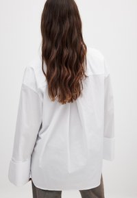 Witte lange mouw blouse met een relaxed fit, voorzien van een klassieke kraag en brede cuffs. Gladde textuur met een lichte glans.