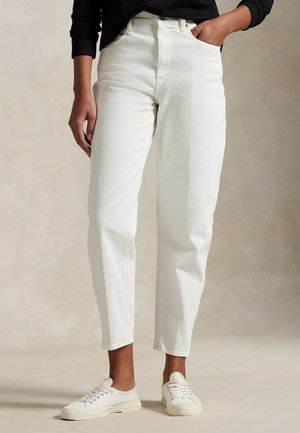 Modèle portant un jean blanc à coupe droite, un haut noir et des baskets blanches, une main dans une poche.