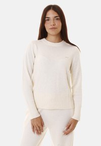 Maglione bianco lavorato a maglia con scollo e polsini a coste, caratterizzato da un motivo testurizzato e un piccolo logo sul petto.
