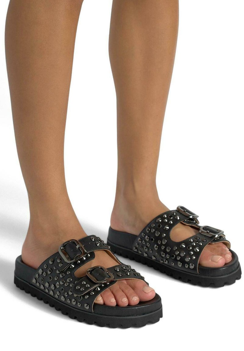 Black slide sandals with two buckles and studded detailing. Features a textured sole and cutouts on the upper part for breathability.