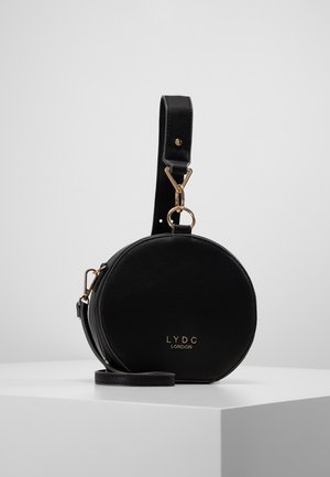 Czarna okrągła torebka wykonana ze skóry z odpinanym paskiem, ozdobiona złotymi metalowymi elementami i tłoczonym logo na przodzie.