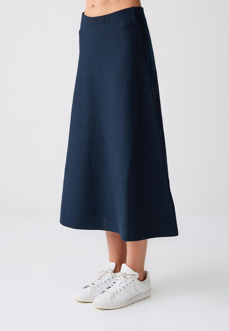 Marineblauwe A-lijn midirok gedragen met witte veterschoenen, getoond van taille tot voeten tegen een effen lichte achtergrond.