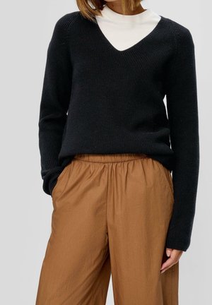 Zwarte geribbelde gebreide trui met een V-hals ontwerp en lange mouwen, gecombineerd met bruine broek met elastische taille. Textuurstof in een relaxte pasvorm.