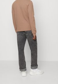 Beige strukturierte Langarmbluse, graue Jeanshose mit hochgekrempelten Säumen und weiße Sneakers. Einfaches Design mit sichtbaren Nähten.