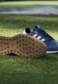 Le scarpe sportive blu presentano una tomaia in pelle scamosciata e materiali sintetici, tre strisce bianche e una suola in gomma testurizzata con tacchetti rotondi per una migliore trazione.