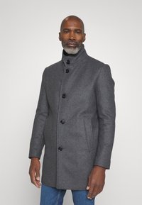 Cappotto di lana grigio scuro con colletto alto, dotato di sei bottoni neri e tasche laterali, vestibilità sartoriale e superficie liscia.