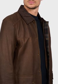 Chaqueta de cuero marrón con cuello de pana, con un forro a cuadros y detalles de botones de presión en la parte delantera y los bolsillos.