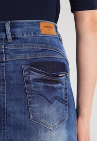 Jeans i denim i medelblått med ett lädermärke märkt "cream", synlig bakficka med zigzag-söm och urblekt textur.