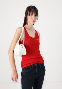 Débardeur rouge à côtes avec un col rond, associé à un jean noir et un petit sac à main en cuir blanc avec fermeture éclair.