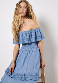 Blaues Off-Shoulder-Kleid mit schichtigen Rüschen, Spitze-Details und einem gerafften Bund, das ein lockeres, fließendes Design und eine weiche Textur aufweist.