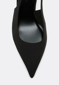 Chaussure plate noire à bout pointu avec une semelle intérieure lisse et une tige en tissu présentant une bride découpée sur un côté.