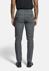 Šedé, strukturované kalhoty slim fit s elastickým pasem a dvěma zadními kapsami se zapínáním na knoflíky. Nohavené s černými botami.