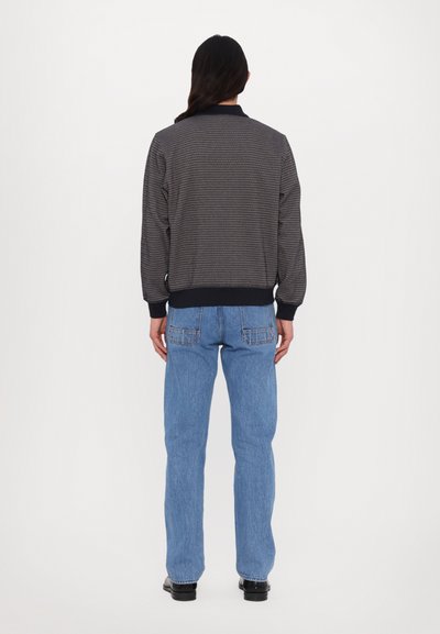 Γκρι σακάκι με μοτίβο και μαύρο γιακά, ελαστικούς μανίκους και ζώνη, συνδυασμένο με ανοιχτό μπλε παντελόνι καμπάνα και μαύρες μπότες.