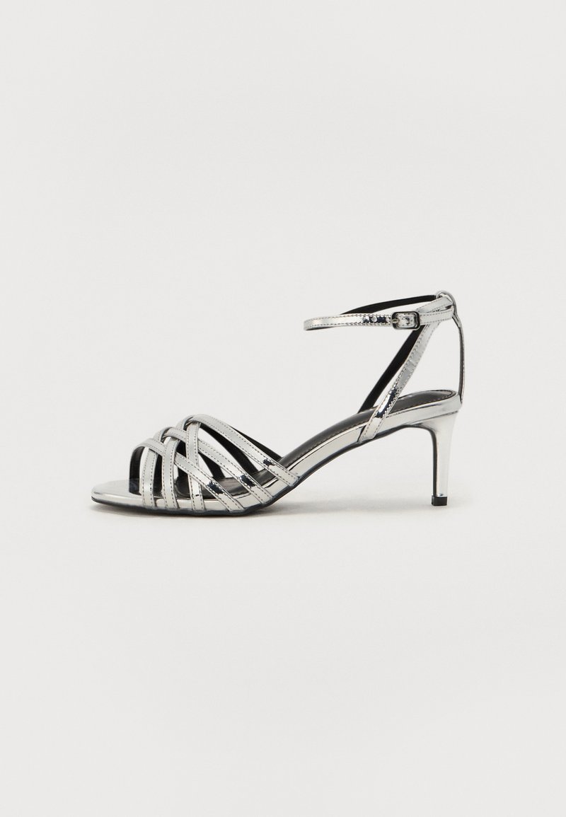 Sandales à talons hauts argentées avec des lanières croisées, une boucle à la cheville et un design à bout ouvert sur une finition lisse et brillante.