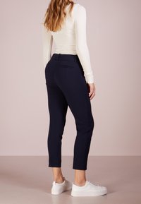 Granatowe spodnie 3/4 o slim fit, z tylnymi kieszeniami i gładką fakturą, w połączeniu z białymi sneakersami i dopasowaną bluzką z długim rękawem.