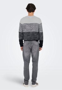 Suéter de punto a rayas grises y negras con mangas largas, combinado con vaqueros grises y zapatillas blancas, visto desde atrás.