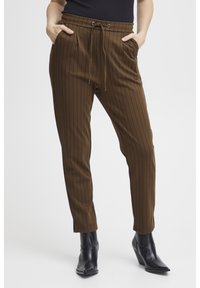 Donkerbruine gestreepte broek met een tapered fit, elastische tailleband en trekkoord. Bevat zijzakken en ribbelstructuur. Gecombineerd met zwarte enkelboots.