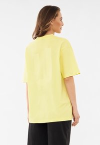 Żółta, oversize koszulka wykonana z miękkiej bawełny, z dużym, wyblakłym logo na plecach. Krótkie rękawy i okrągły dekolt.