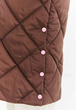 Brązowa pikowana tkanina z ukośnym przeszyciem i czterema równomiernie rozmieszczonymi okrągłymi różowymi zatrzaskami wzdłuż szwu.