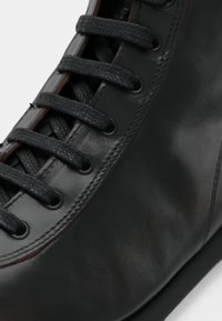 Černá kožená bota s texturovaným povrchem, tmavými tkaničkami, hladkou špičkou a kontrastním hnědým prošitím podél švů.