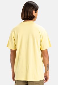 Camiseta de algodón amarilla de manga corta con cuello redondo y corte relajado, que presenta una textura suave y una parte trasera lisa sin diseños.