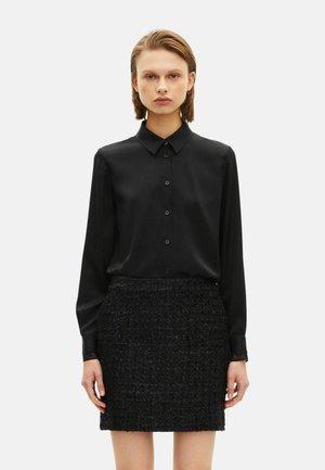 Chemise noire à manches longues avec devant boutonné et col pointu, associée à une mini-jupe noire texturée avec un motif tissé.