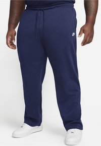 Námořnické tepláky s elastickým páskem, bočními kapsami a bílým logem Nike. Materiál má hladkou texturu a volný střih.