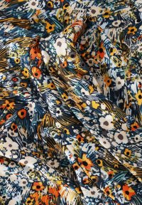 Tessuto colorato con un denso motivo floreale che presenta fiori bianchi, arancioni e gialli su sfondi astratti blu scuro e verdi.