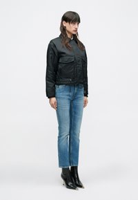 Μαύρο κοντό σακάκι με δύο μπροστινές τσέπες, συνδυασμένο με μπλε τζιν μεσαίου ύψους και μαύρα μπότες αστραγάλου με τακούνι. Ομαλή υφή υφάσματος.