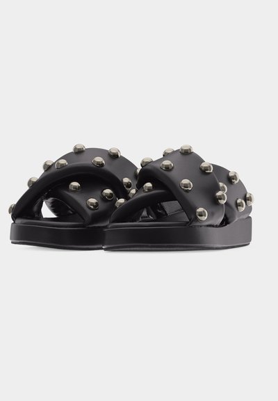 Sandales en cuir noir à enfiler avec de larges lanières croisées ornées de clous ronds argentés et semelles plates.