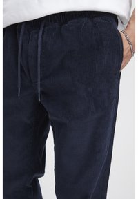 Tmavomodré kordurové nohavice so zvislou ryhovanou textúrou, elastickým pásom so šnúrkou na stiahnutie a bočnými vreckami.