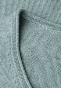 Hellblau gestrickter Pullover mit strukturiertem Finish, tiefem V-Ausschnitt und gerippten Kanten. Weicher Stoff, der ein zartes Muster zeigt.