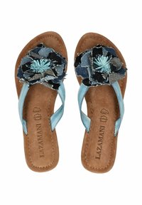Blaue Lederflip-Flops mit einem Denim-Blütenakzent auf einem braunen Wildlederfußbett, mit hellem Stich und offener Zehenpartie.