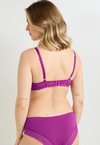 Set di reggiseno e slip abbinati con bordo in pizzo viola. Spalline regolabili e chiusura a gancio. Tessuto liscio con dettagli in pizzo floreale. Vista sul retro.