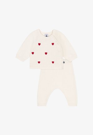 Ensemble pour bébé en tricot crème comprenant un pull à manches longues avec des appliqués en forme de cœurs rouges et des boutons sur le côté, associé à un pantalon texturé assorti.