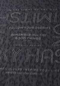 Tejido con un patrón texturizado en negro; presenta piedras brillantes de color plateado que forman textos y frases motivacionales en varias fuentes y tamaños.