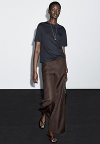 Marineblå kortærmet top kombineret med brede brune bukser. Outfit'et har en glat tekstur, minimalistisk design og diskret smykkeaccent.