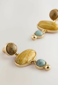 Goldfarbene Ohrringe mit drei Edelsteinen: einem großen ovalen gelben Stein, einem kleineren ovalen blauen Stein und einem runden braunen Stein.