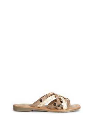 Flad sandal med beige flettede og ruskindssnore, dekoreret med runde metalnitter og en brun sål.