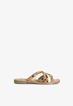 Flad sandal med beige flettede og ruskindssnore, dekoreret med runde metalnitter og en brun sål.