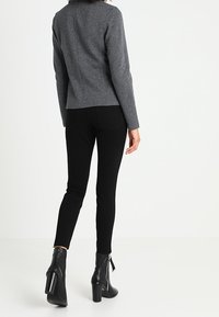 Šedá přiléhavá bunda s dlouhými rukávy, hladkou texturou a detailem zadního švu, kombinovaná s černými úzkými džíny a kotníkovými botami.