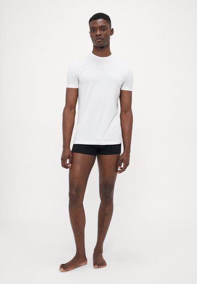 Weißes T-Shirt mit kurzen Ärmeln und einer enganliegenden Passform, kombiniert mit schwarzen Shorts. Glatte Textur und minimalistische Details, entworfen für Komfort und Bequemlichkeit.