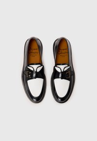 Mocasines de cuero en blanco y negro con una hebilla decorativa y punta redonda, con una textura suave y plantilla marrón.